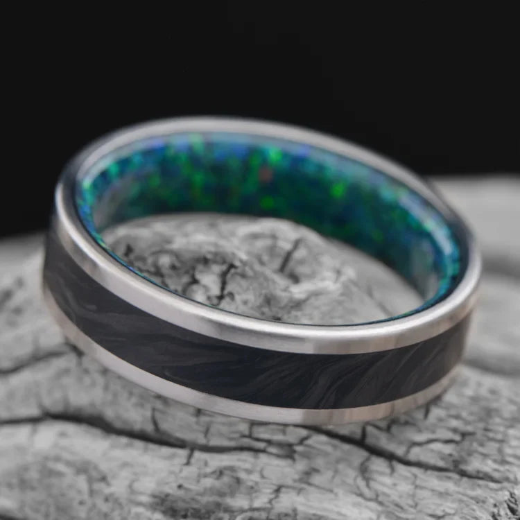 Titanium wedding band with central forged inlay and black emerald opal sleeve, 6mm mens ring, unique design, free engraving, displayed on a white sea branch.