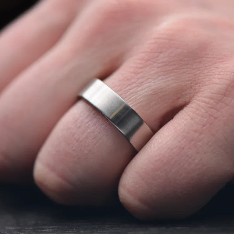 Mens titanium wedding band with 10K rose gold inner sleeve, featuring a brushed flat profile, shown on a hand; 7mm unique mens ring with free engraving option.