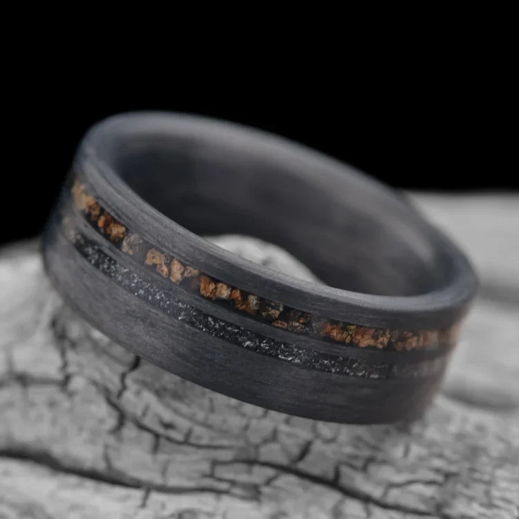 Unidirectional mens wedding ring with crushed T-Rex and meteorite inlays, 7mm band, unique design, free engraving, displayed on white sea branch.