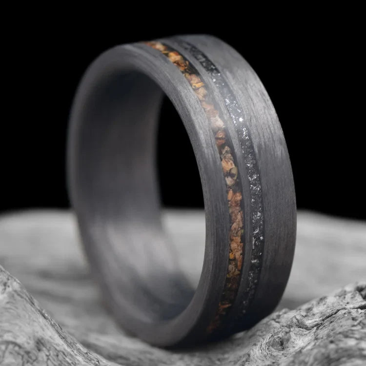 Unidirectional mens wedding ring with crushed T-Rex and meteorite inlays, 7mm band, unique design, free engraving, displayed on a white sea branch.