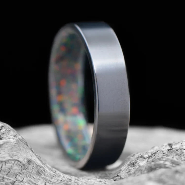 Black Titanium Wedding Band with Black Emerald Opal Inner Sleeve, 6mm Mens Wedding Ring, Polished Flat Profile, displayed on a white sea branch, free engraving available.