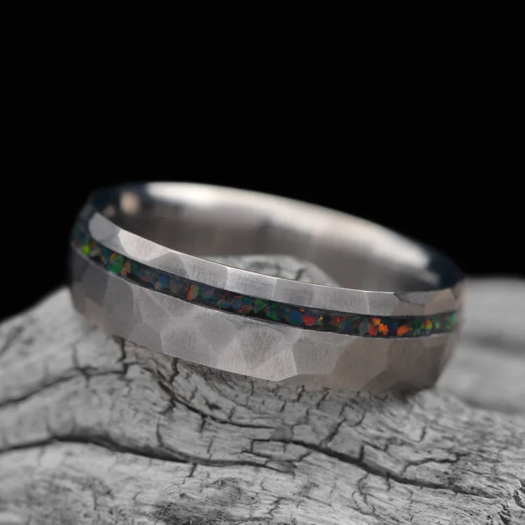 Titanium wedding band with black fire opal inlay, featuring free engraving, 6mm mens faceted domed ring, unique mens wedding band displayed on a white sea branch.