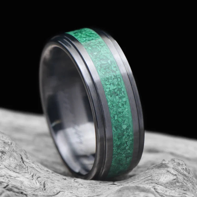 Black titanium wedding band with central malachite inlay, 7mm mens ring, unique design, free engraving, displayed on white sea branch.