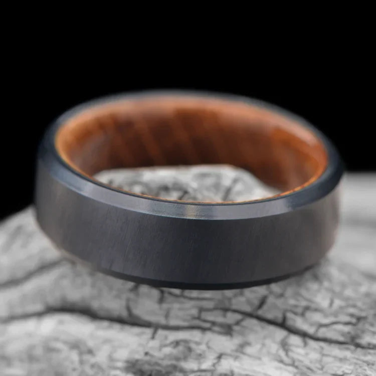 Black Titanium Wedding Band with Whiskey Barrel Oak Inner Sleeve, 7mm Mens Wedding Ring, Unique Design, Free Engraving, displayed on white sea branch background.