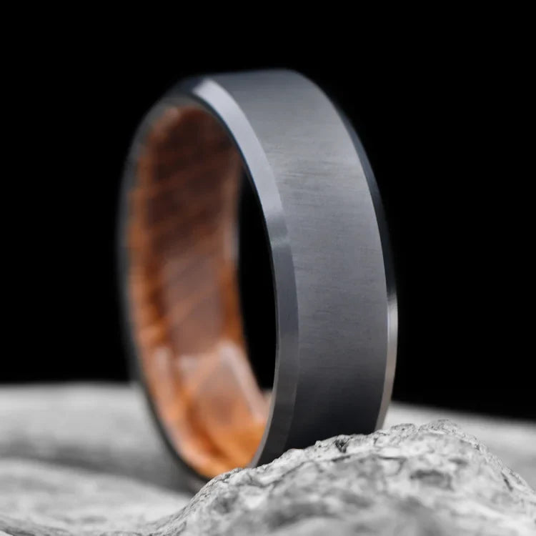 Black Titanium Wedding Band with Whiskey Barrel Oak Inner Sleeve, 7mm Mens Wedding Ring, Unique Design, Free Engraving, displayed on a white sea branch.