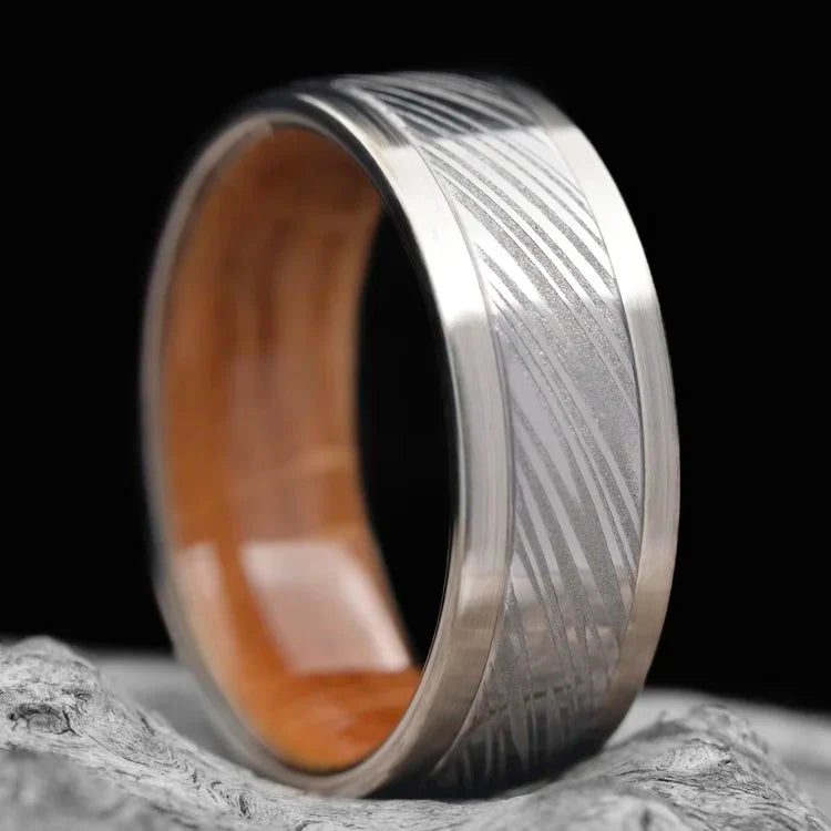 14K white gold wedding band with central Heimskringla inlay, whiskey barrel oak inner sleeve, 9mm width, mens polished finish, free engraving, displayed on white sea branch background.