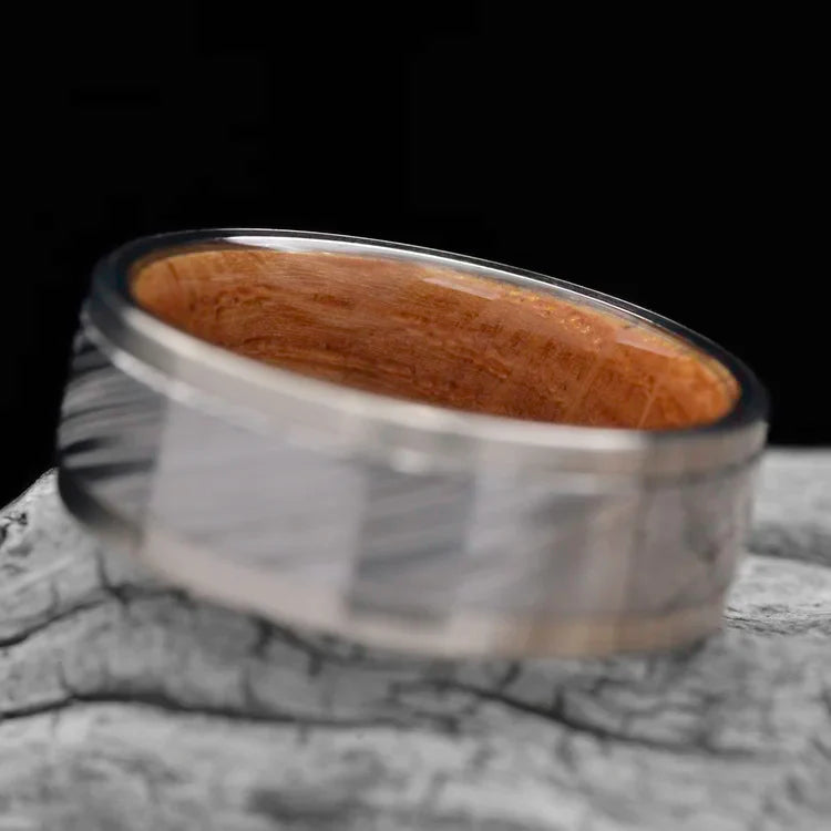 14KW mens wedding band with central Heimskringla inlay and whiskey barrel oak inner sleeve, 9mm polished finish, displayed on a white sea branch, free engraving available.