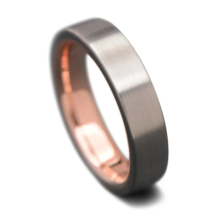 Titanium wedding band with 10K rose gold inner sleeve, free engraving, 5mm width, simple custom ring with brushed flat profile on white background.