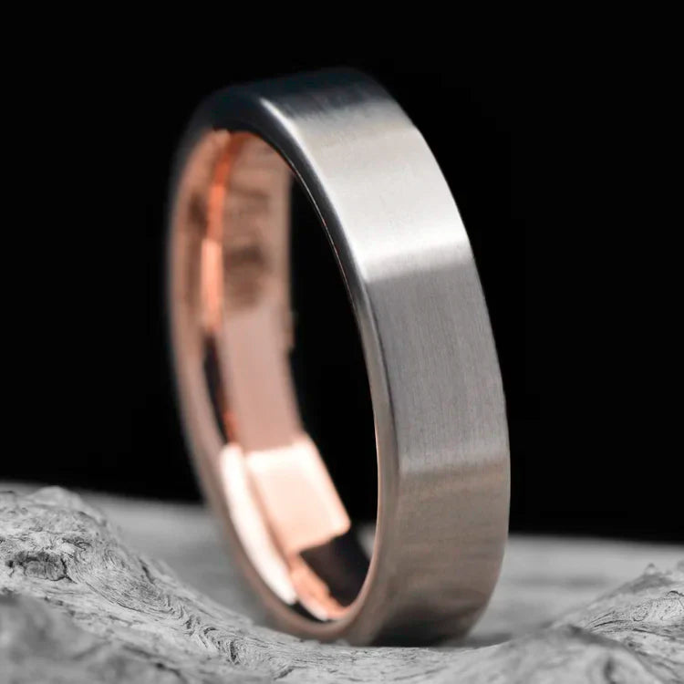 Titanium wedding band with 10K rose gold inner sleeve, 5mm brushed flat profile, laying on white sea branch, free engraving available, simple custom design.