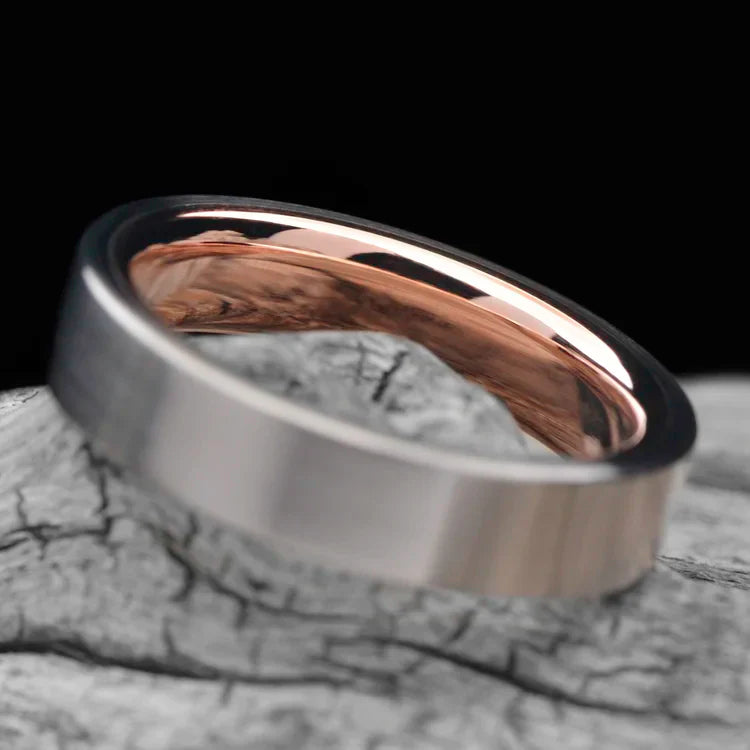 Titanium wedding band with 10K rose gold inner sleeve, featuring a brushed flat profile, 5mm width, simple custom design, free engraving, displayed on a white sea branch.