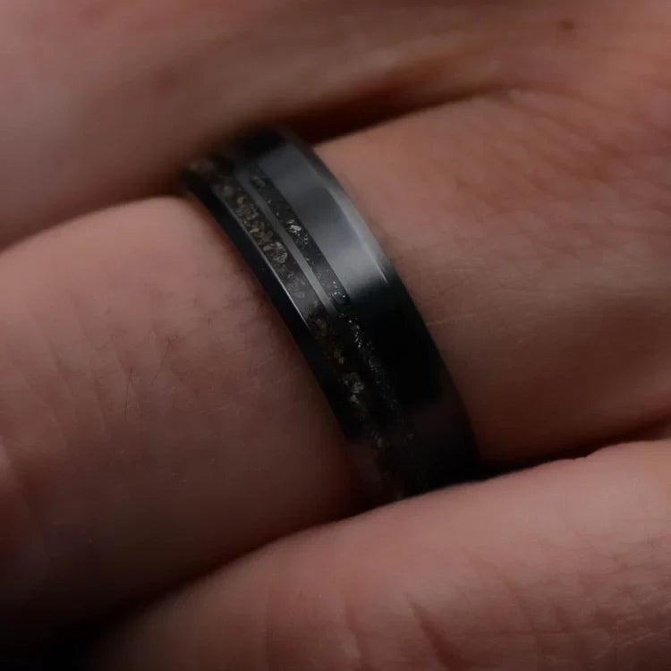 Mens black titanium wedding band with crushed T-Rex and meteorite inlays, featuring a WW2 rifle inner sleeve, shown on a hand; unique 7mm design with free engraving option.