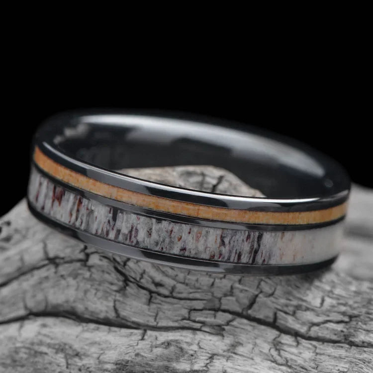 Black titanium wedding band with deer antler and birds eye maple inlays, 6mm mens ring, polished flat profile, free engraving, displayed on a white sea branch.