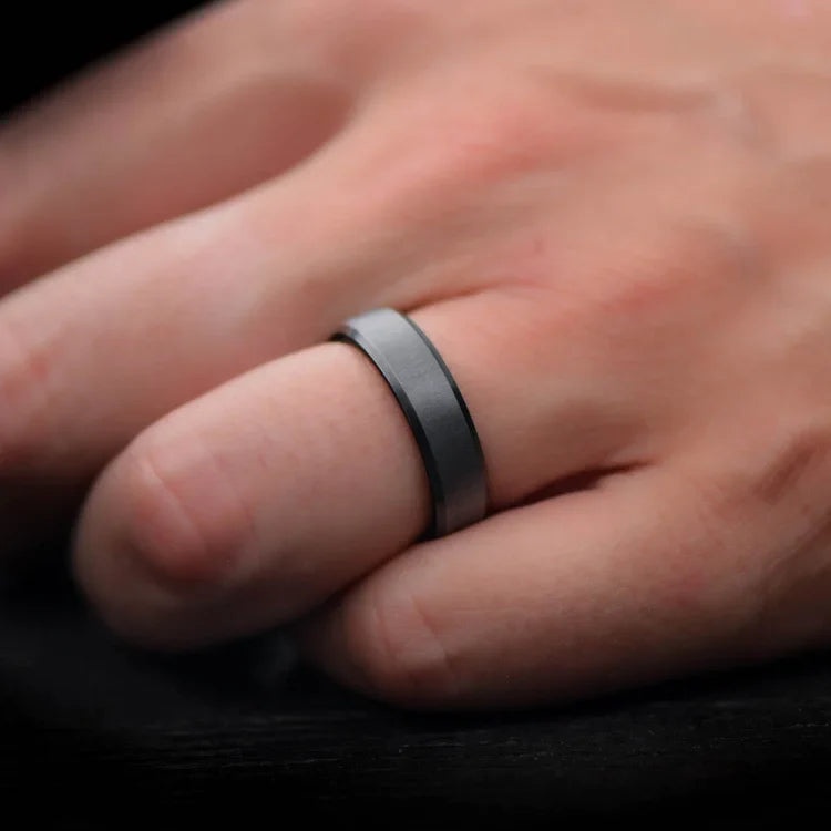 Mens 6mm black titanium wedding band with koa wood inner sleeve, featuring a brushed bevel profile, shown on a hand; includes free engraving.