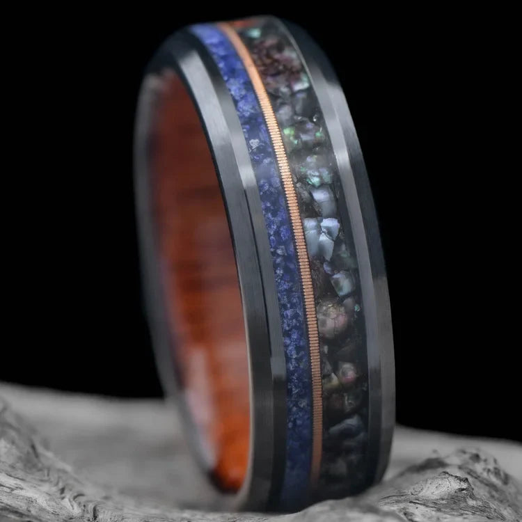 Black titanium wedding band featuring black pearl, lapis lazuli, and guitar string inlays, displayed on a white sea branch, 7mm unique mens wedding ring with free engraving.