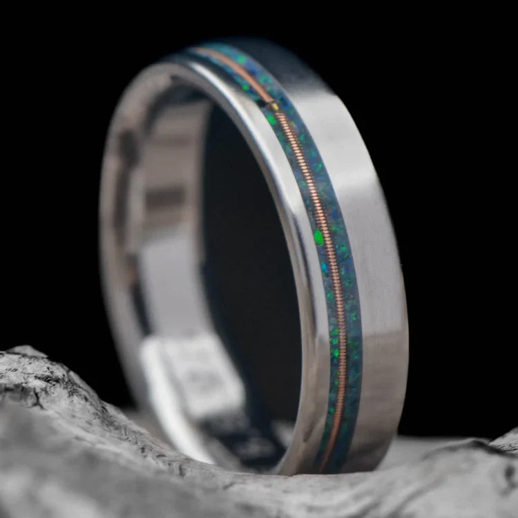 Titanium wedding band with emerald opal and guitar string inlay, custom flat profile, 5mm unique wedding ring, free engraving, displayed on a white sea branch.