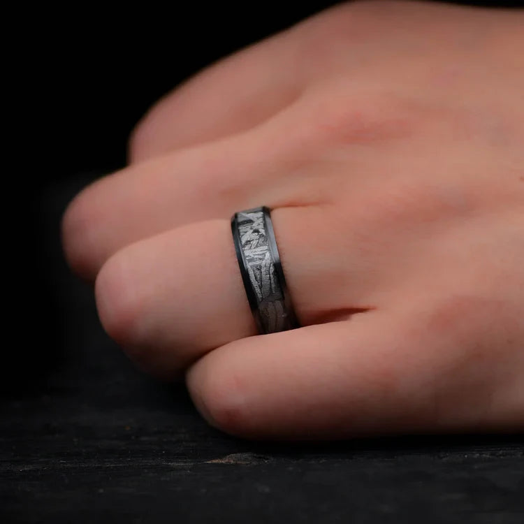 Mens wedding band featuring a black titanium design with a central meteorite inlay, shown on a hand; unique 7mm ring with free engraving option.