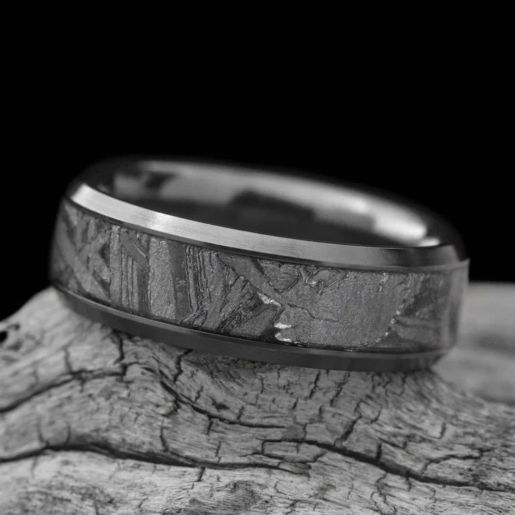 Black titanium mens wedding ring with central meteorite inlay, 7mm wide, featuring free engraving, displayed on a white sea branch.