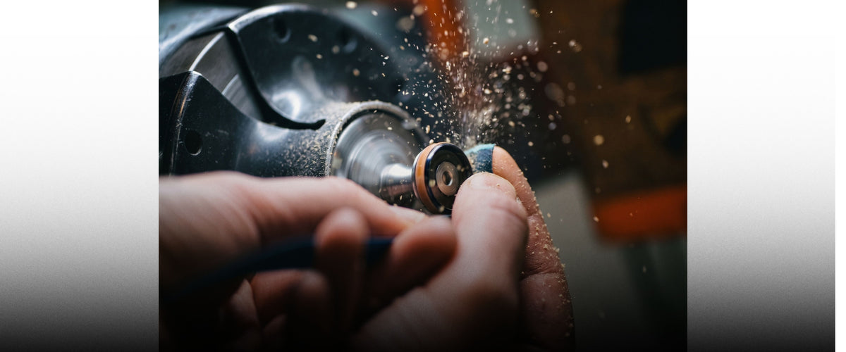 Craftsman's hands shaping a ring on a spinning workshop lathe, sending up a spray of dust