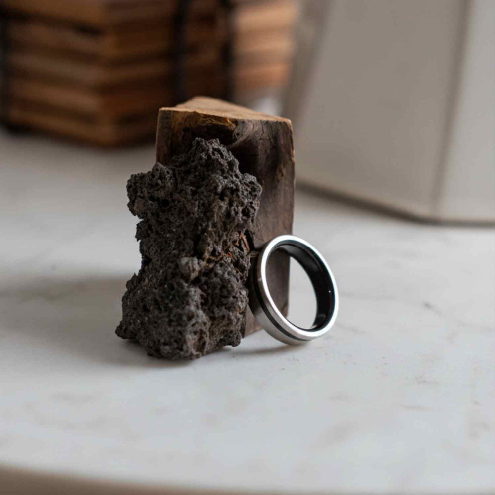 Black custom wedding ring beside a piece of raw lava rock, one of the personal materials Sesto Synergy can set into a band.