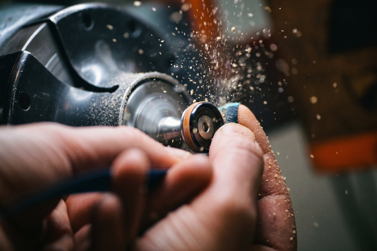 Craftsman's hands shaping a ring on a spinning workshop lathe, sending up a spray of dust