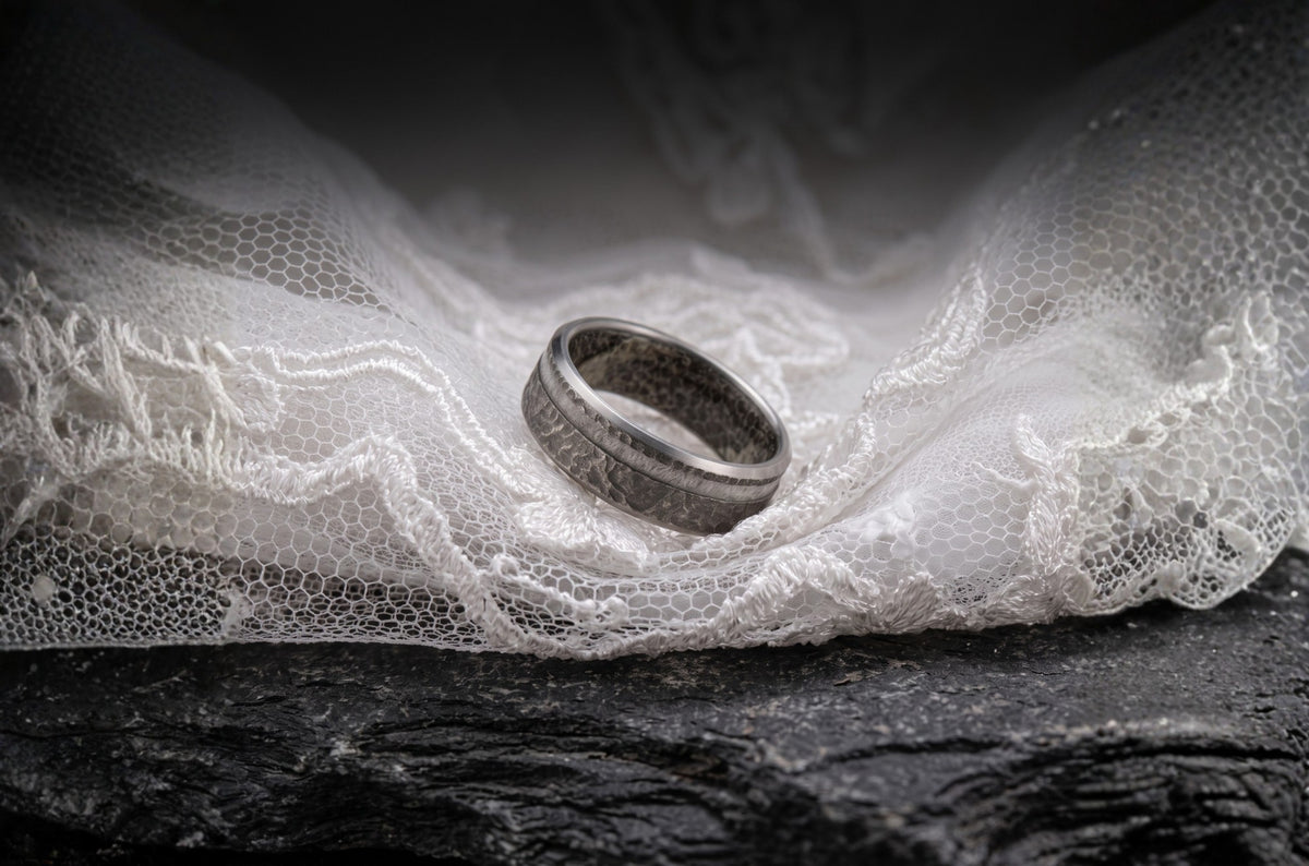 A Sesto Synergy wedding band resting on wedding dress lace over dark slate