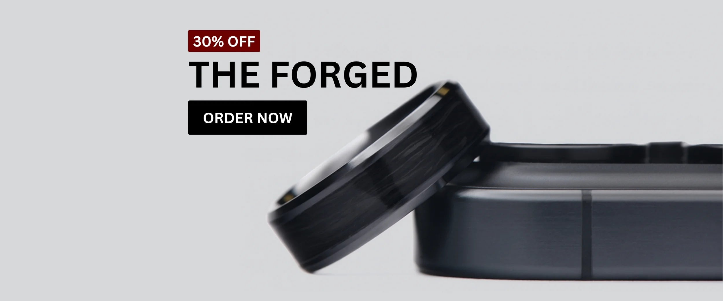 Forged carbon wedding ring from The Forged collection resting on a dark case. Text overlay reads ‘30% Off – The Forged’ with an ‘Order Now’ button on a light grey background